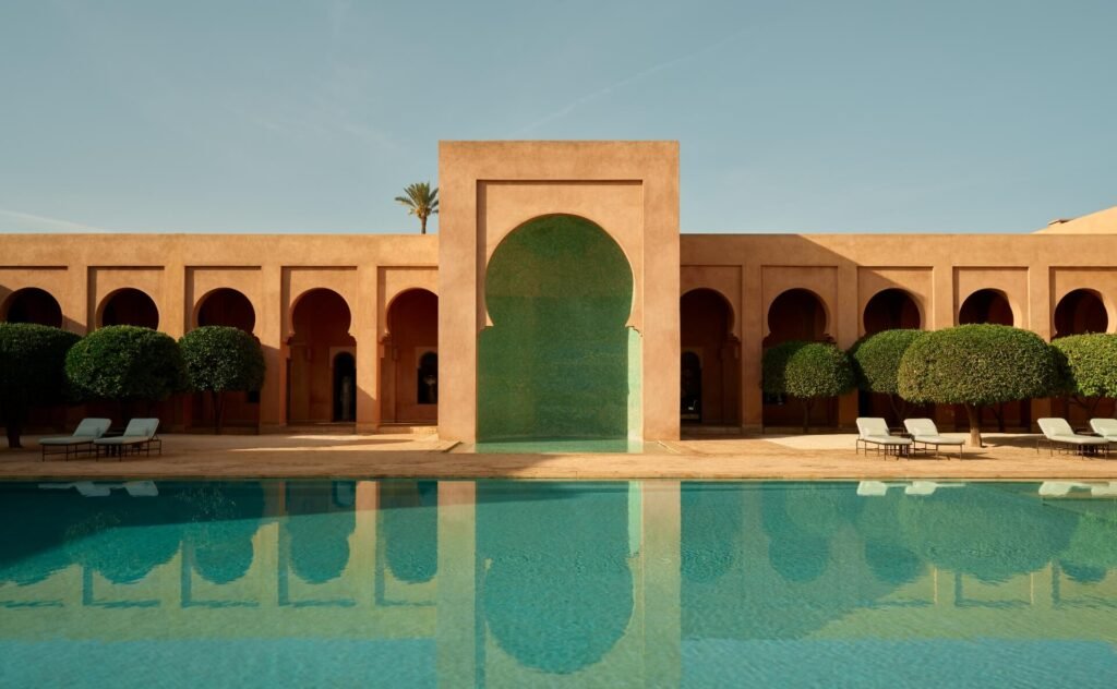 Piscine miroir iconique à Amanjena Marrakech entourée d’architecture rose et de palmiers