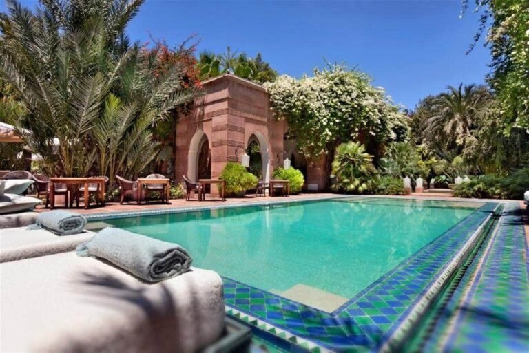 Piscine extérieure entourée de jardins luxuriants et d’une élégante architecture de style palais au Dar Rhizlane à Marrakech.