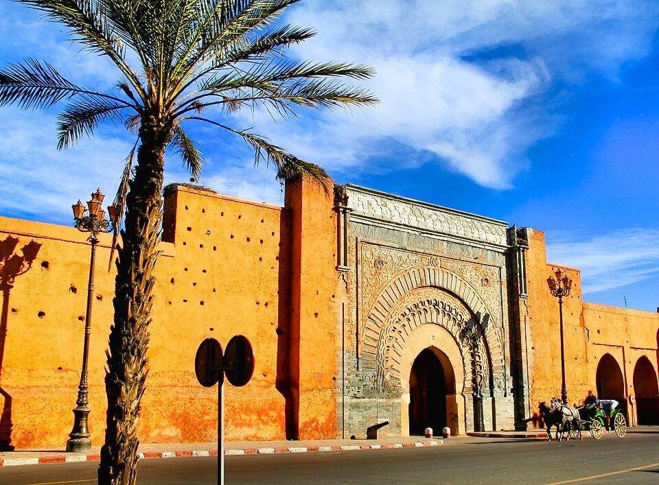 Porte en pierre sculptée dans les remparts ocre de la Médina de Marrakech, avec un palmier et une calèche