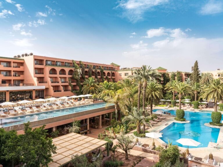 Grande piscine extérieure entourée de palmiers et de jardins luxuriants au Sofitel Marrakech Palais Impérial & Spa.