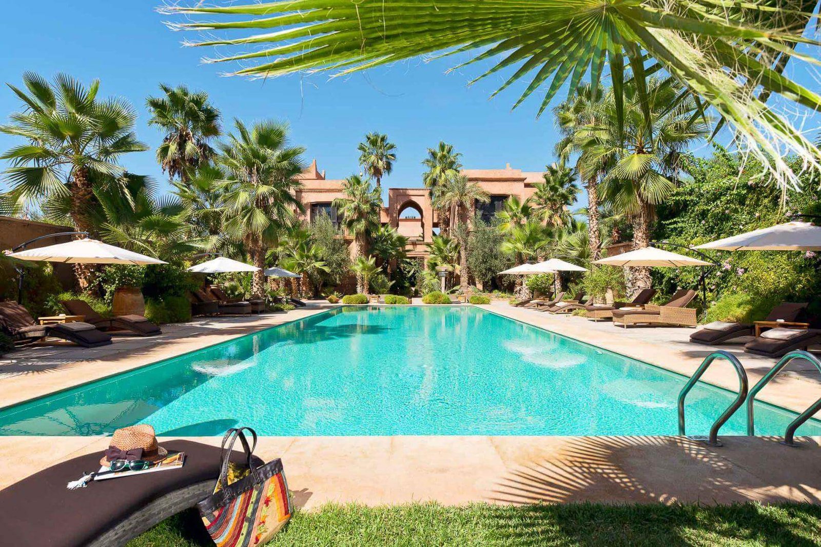 Outdoor swimming pool surrounded by palm trees and lush gardens at Tigmiza Boutique Hotel & Spa in Marrakech.